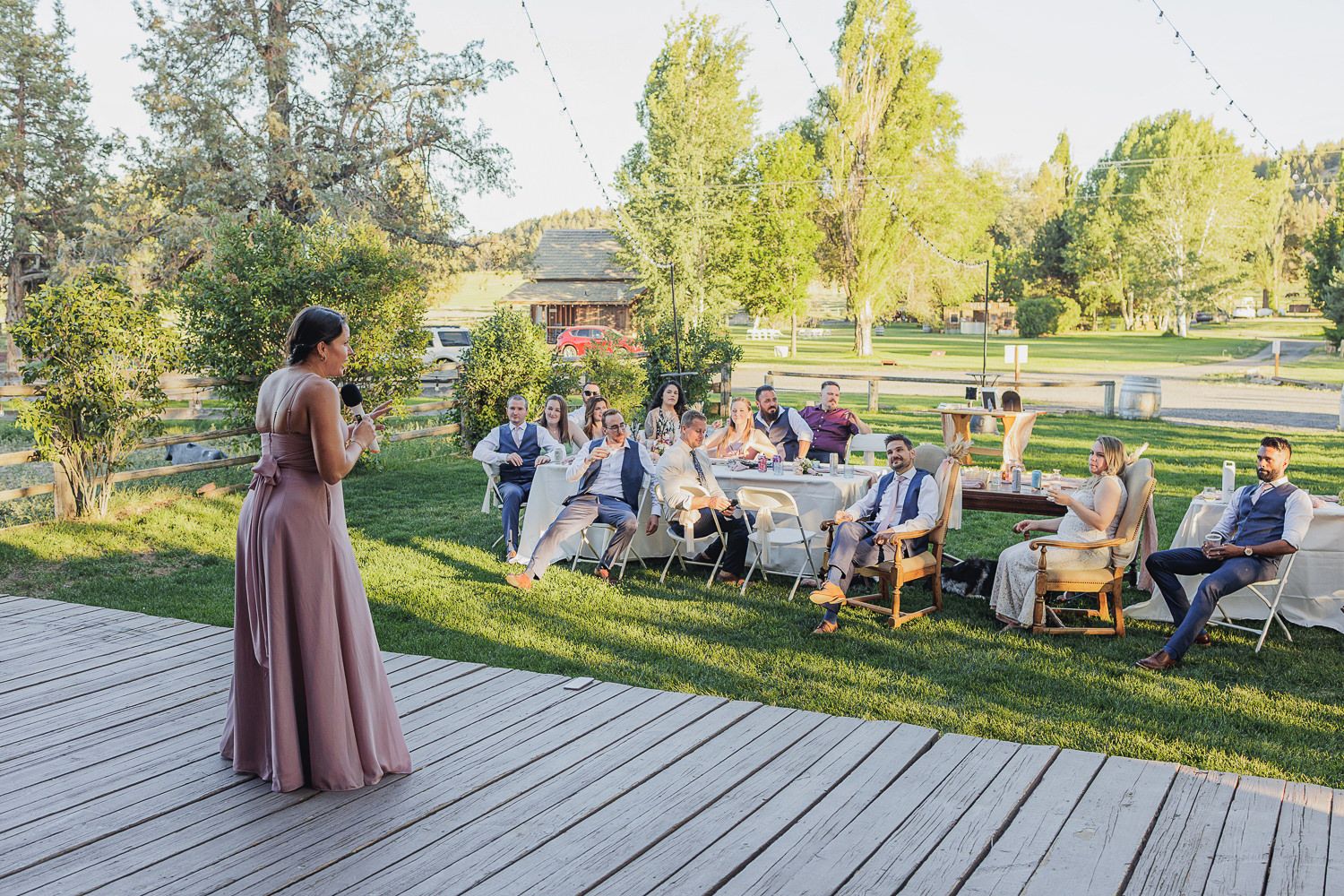 Group of people gathered for an outdoor meditation session on a wooden deck surrounded by green scenery.