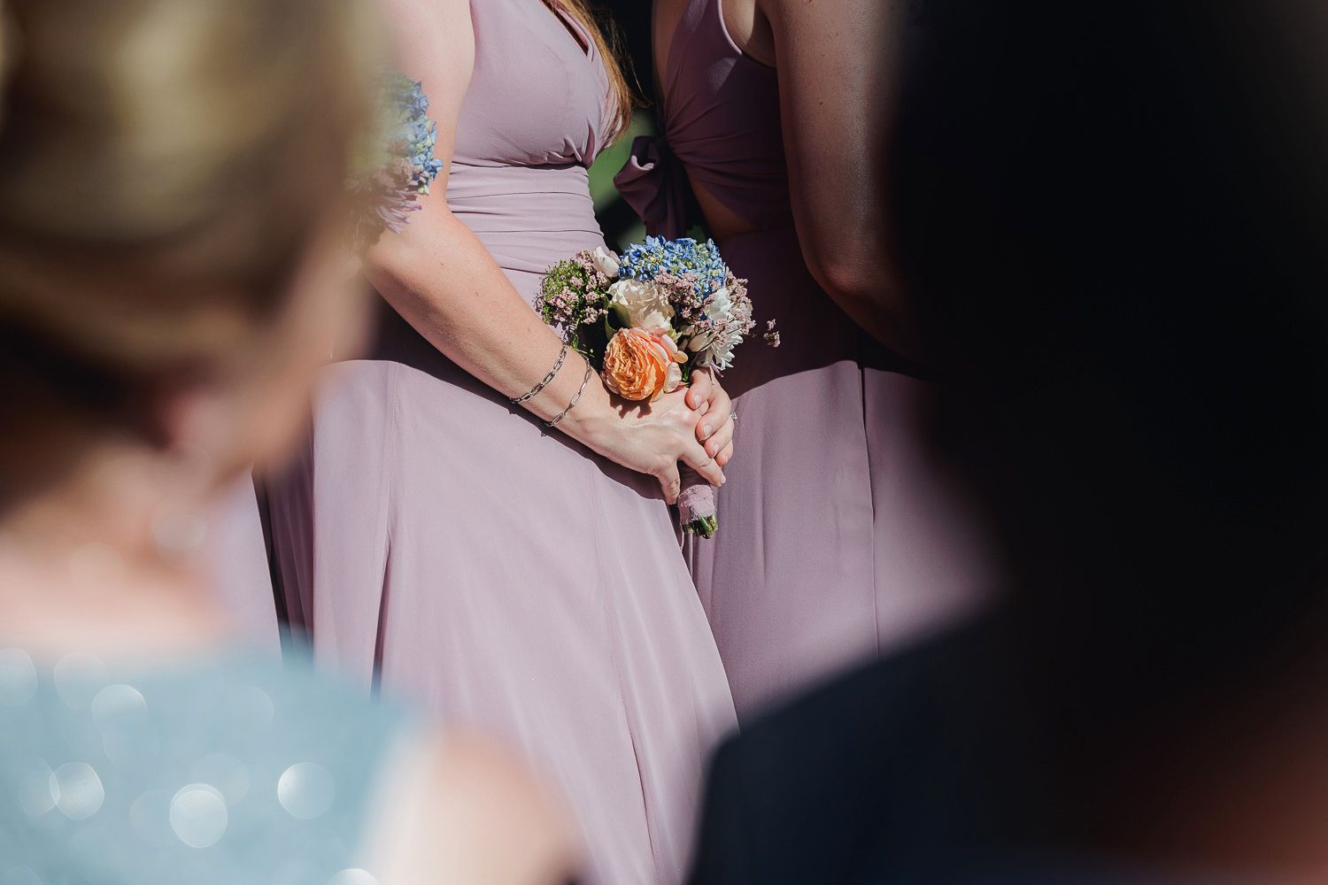 Close-up detail of a bridesmaid holding a delicate floral bouquet against a soft mauve dress.
