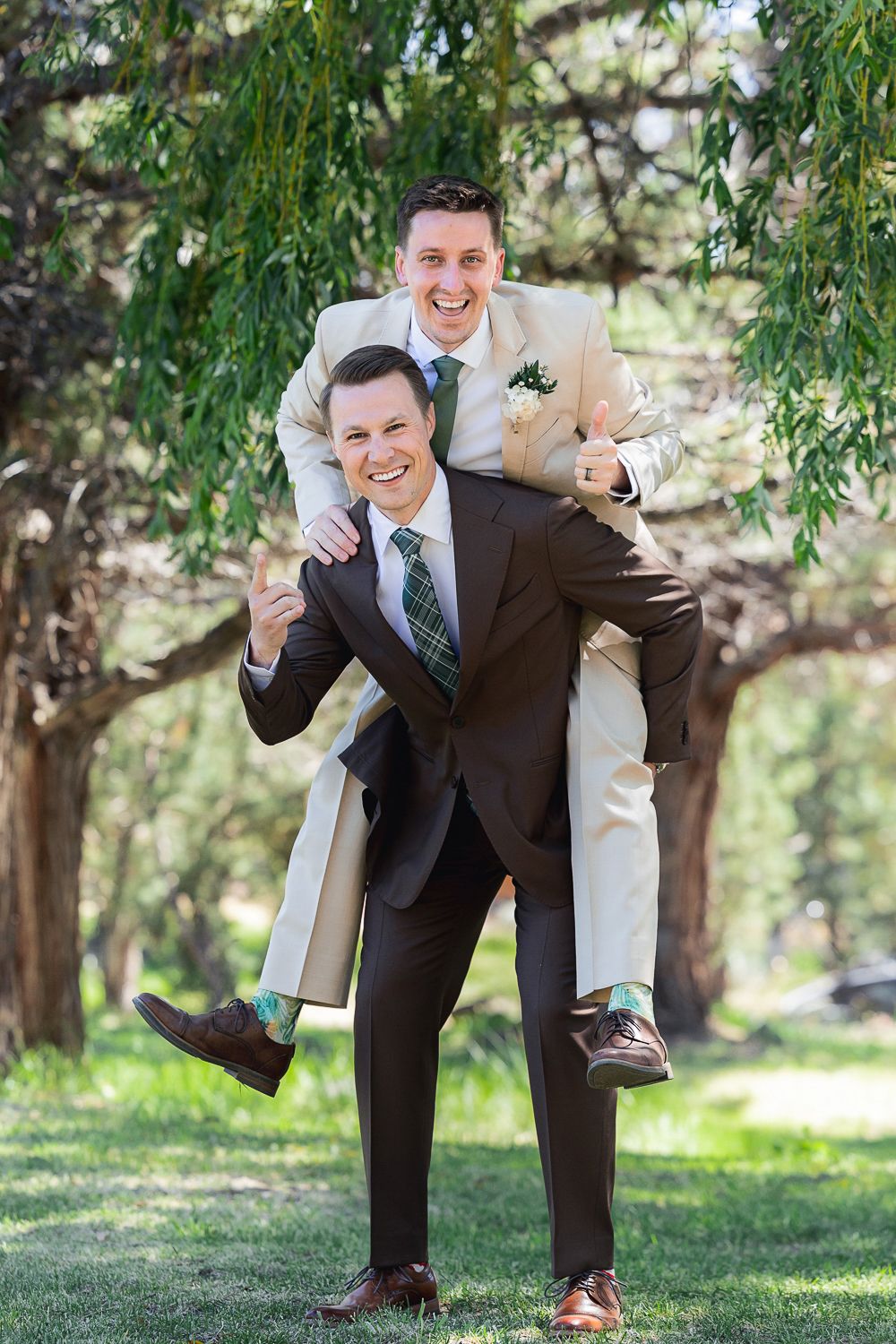 Groomsmen in brown suits strike playful martial arts poses under a willow tree in an outdoor setting.