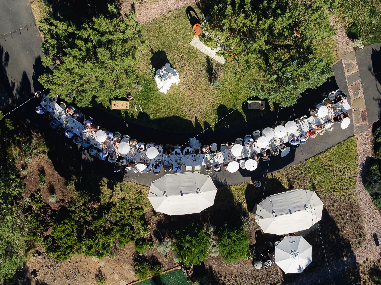Aerial view of wedding reception tables arranged in a curved layout with white umbrellas and outdoor seating.