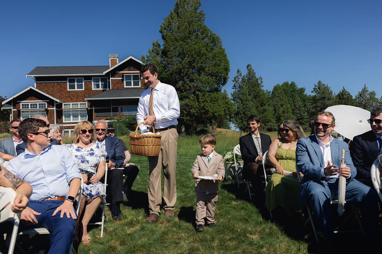 A panoramic outdoor scene shows people gathered in a grassy area near residential homes on a sunny summer day.