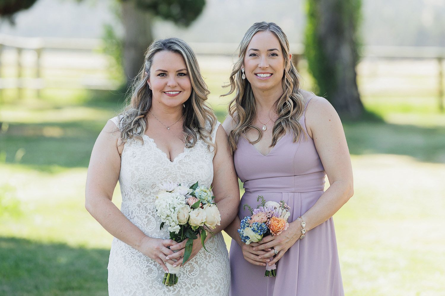 Two wedding party members pose with bouquets against a sunlit outdoor background.