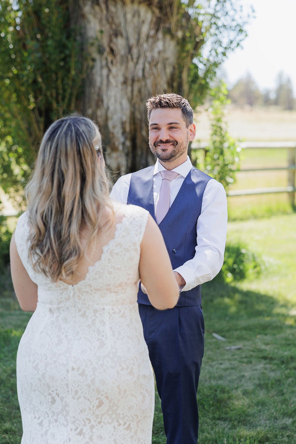 A couple in their wedding attire share an intimate first look moment in a sunlit outdoor garden setting.