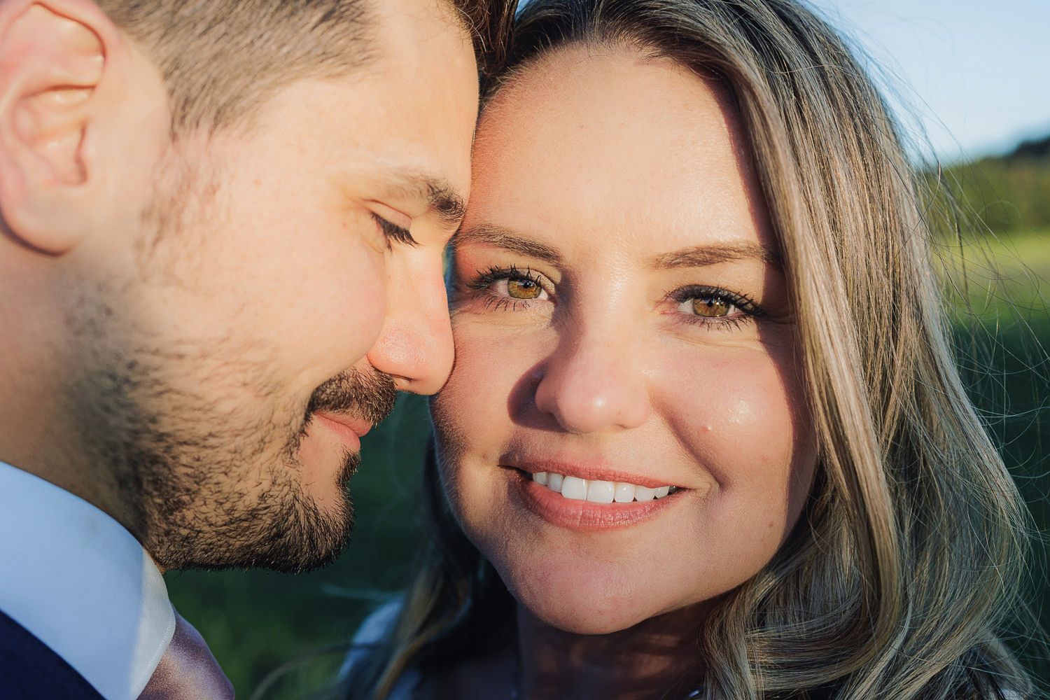 Close-up wedding photography shows a romantic couple in an outdoor setting sharing intimate moments at sunset.