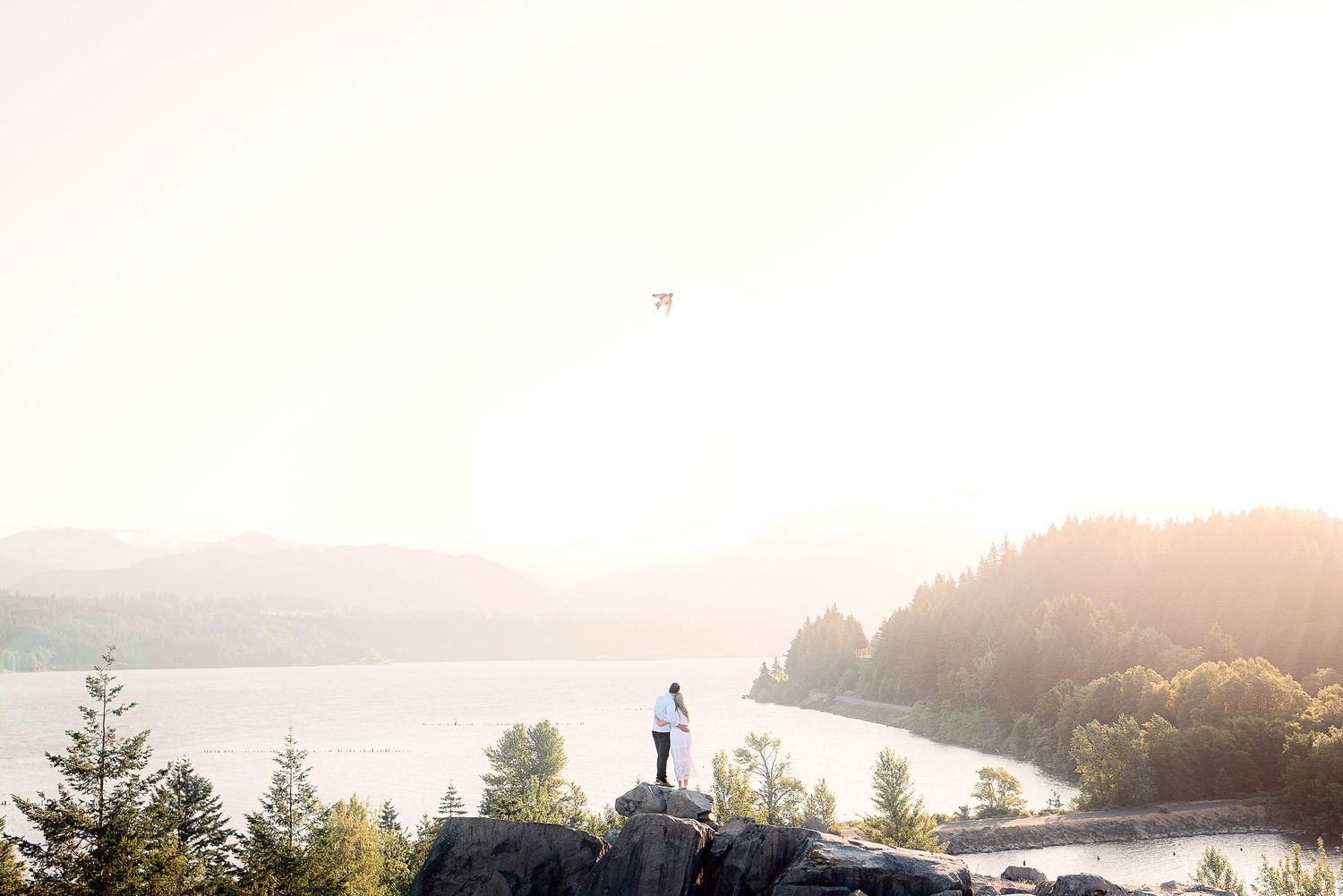 A person stands silhouetted on a rocky outcrop overlooking a misty lake during golden hour sunset.
