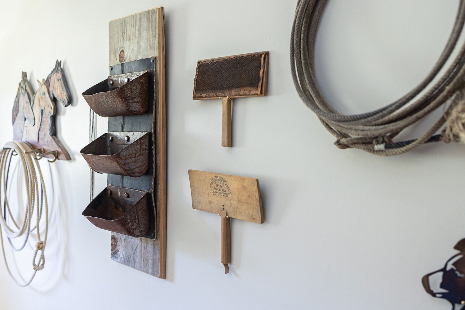Rustic wall display featuring vintage work boots mounted on wooden board with coiled ropes and tools hanging beside them.