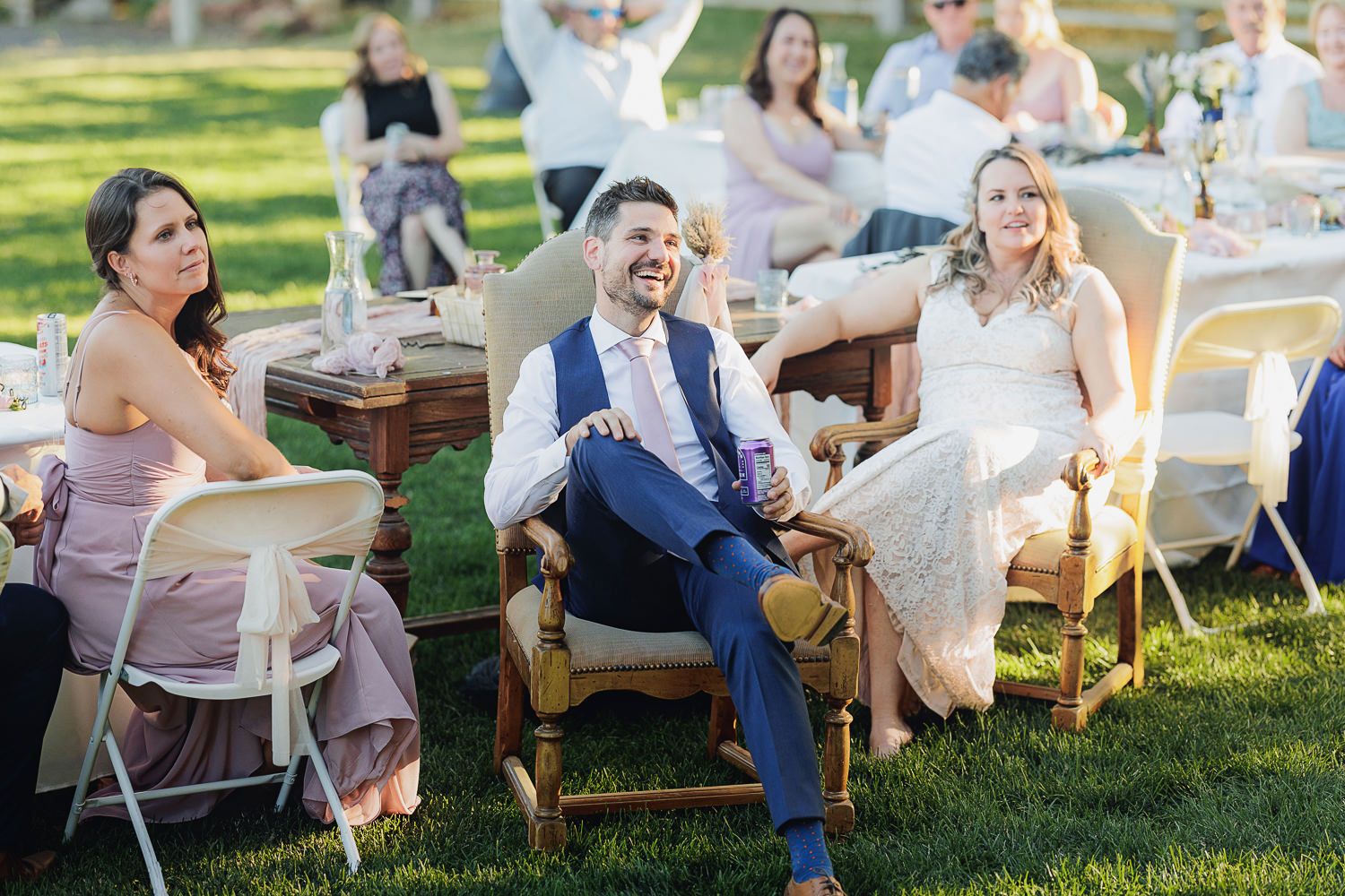 Guests relax on rustic wooden chairs spread across a sunny lawn at an elegant outdoor party setup.