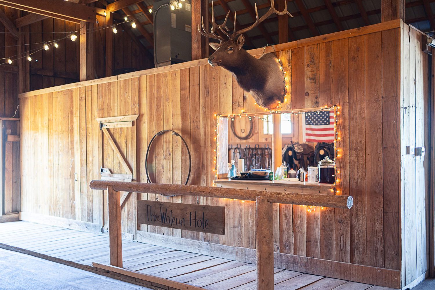 Rustic barn interior with mounted deer head, wooden walls and American flag decoration.
