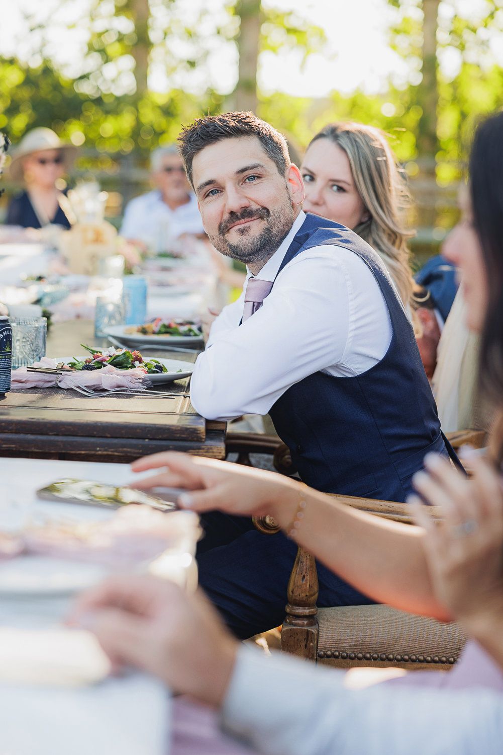 Guests enjoying a meal together at an outdoor dining table on a sunny afternoon.