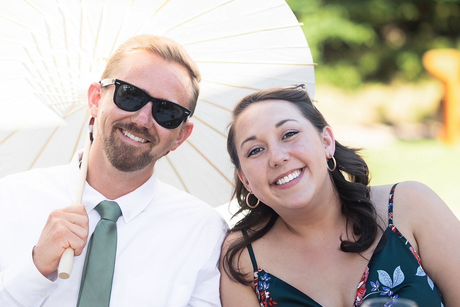A joyful wedding party celebrating in outdoor setting with bouquets and sunlight filtering through trees.