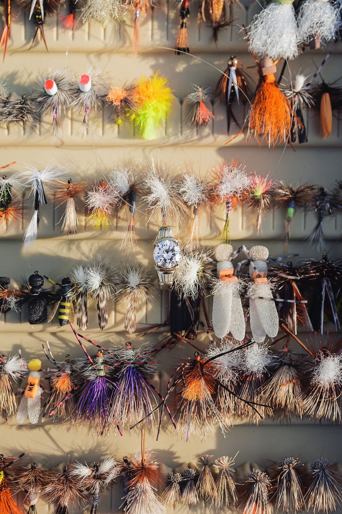 Colorful fishing lures and fly fishing flies displayed on multiple rows showing various feather and tinsel patterns.