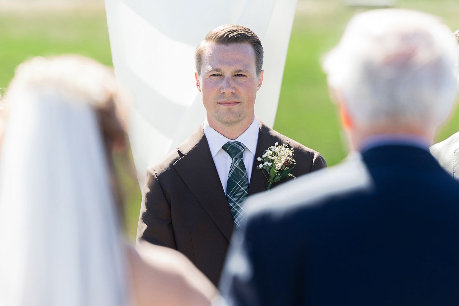 A candid wedding photo shows guests mingling outdoors during a reception with soft natural lighting.