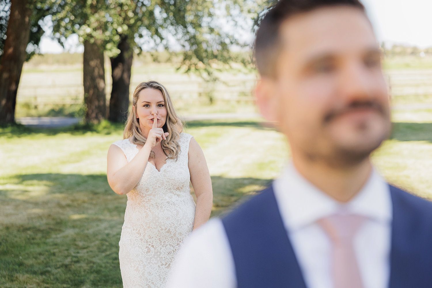A couple in wedding attire stands together outdoors in warm sunlight during their first look moment.