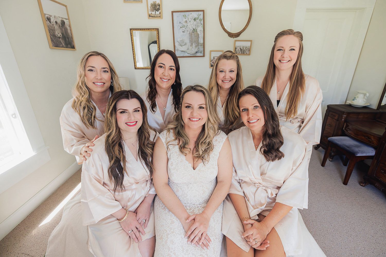 Group wearing matching silk robes pose together while sitting on floor during pre-wedding preparations.