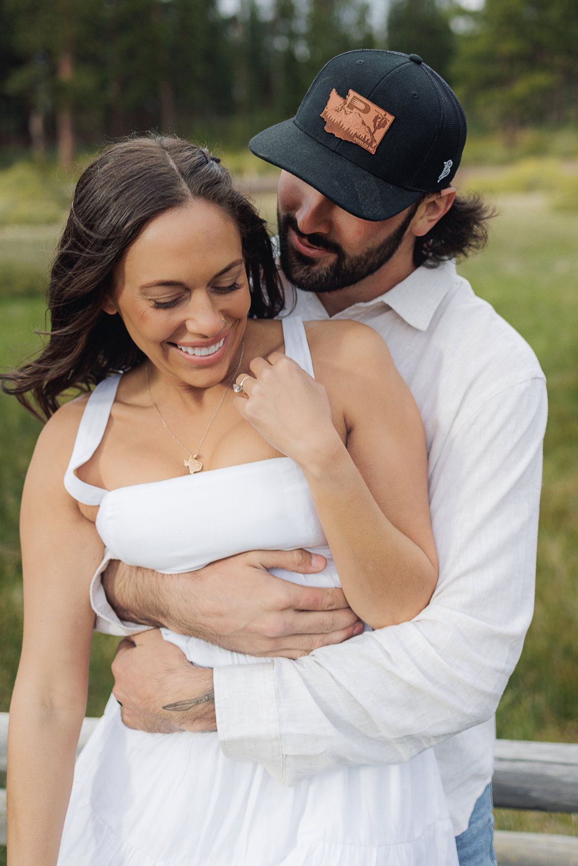 A romantic outdoor portrait shows a couple embracing in soft sunlight against a blurred natural background.