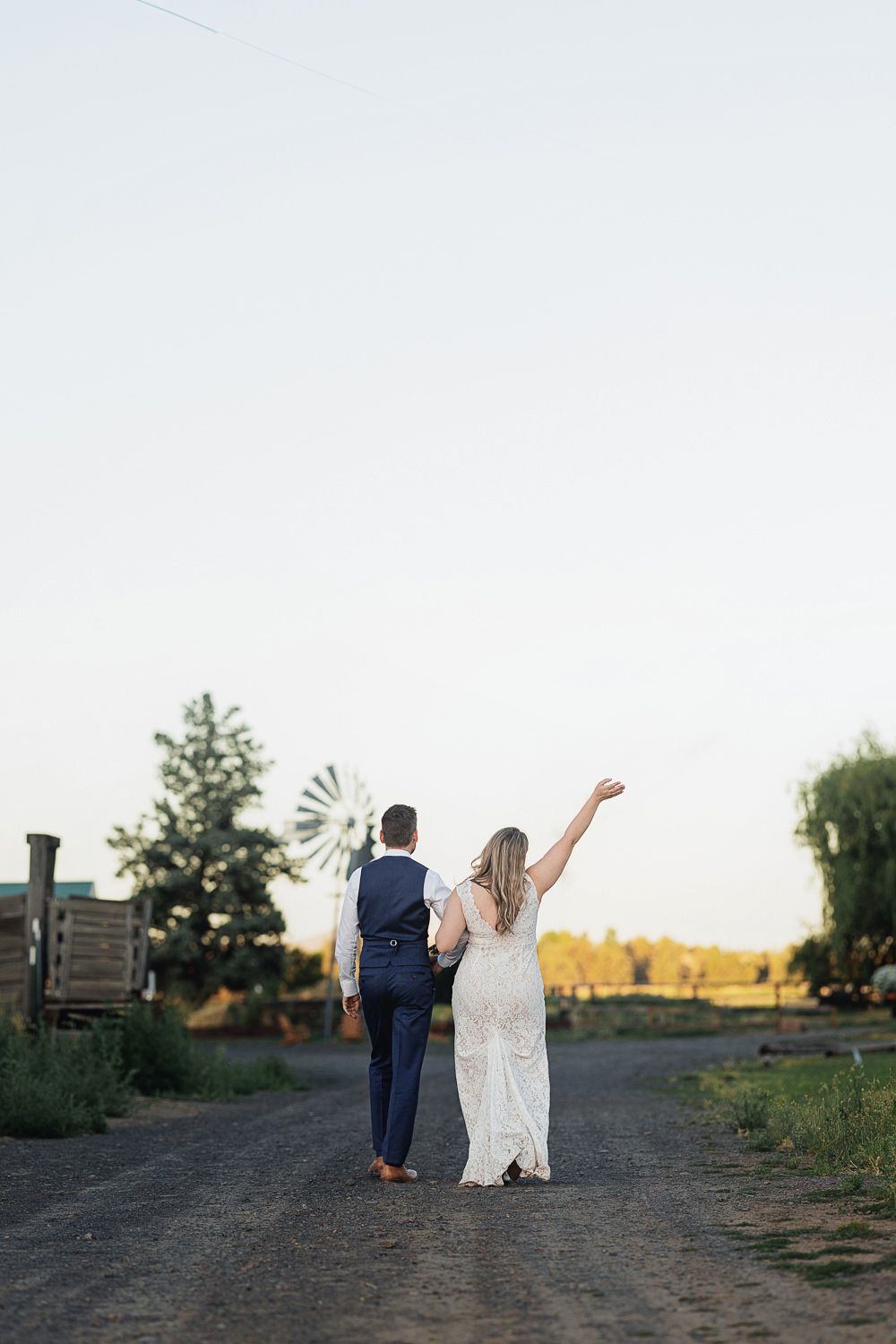 Newlywed couple walks along country path at golden hour in navy suit and white wedding dress.