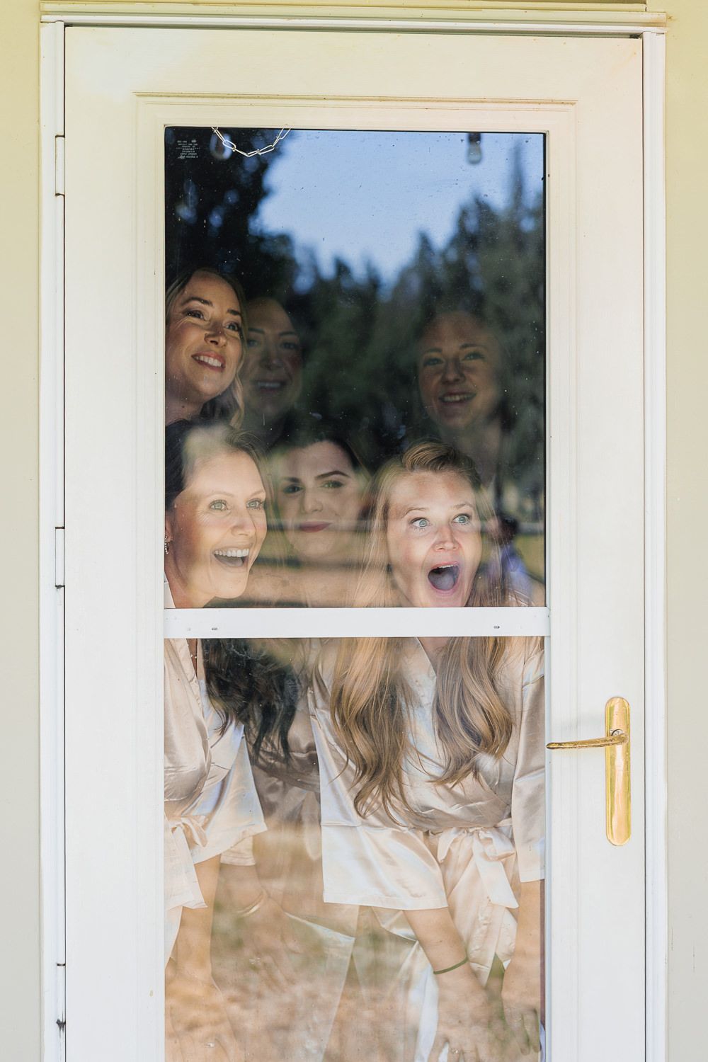 A group of people laughing together while looking through a window, creating a joyful and candid moment.