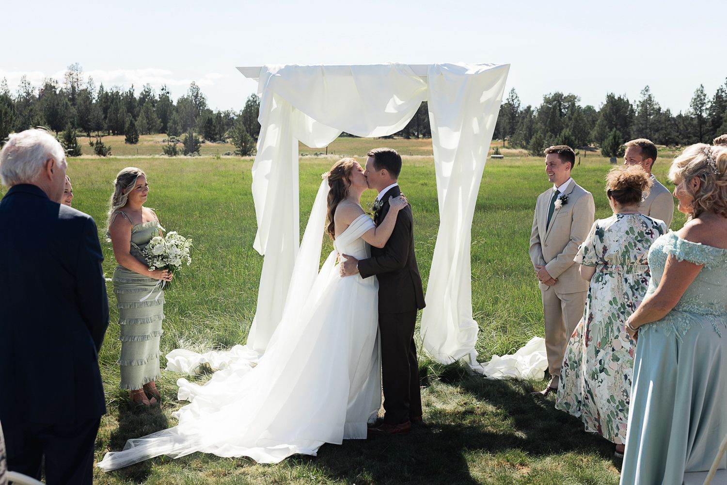 An outdoor wedding ceremony on a grassy hill with white drapery and floral arrangements.