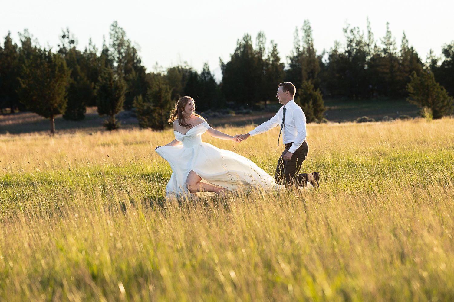 A couple celebrates their wedding day with romantic poses in a sun-lit grassy meadow at golden hour.