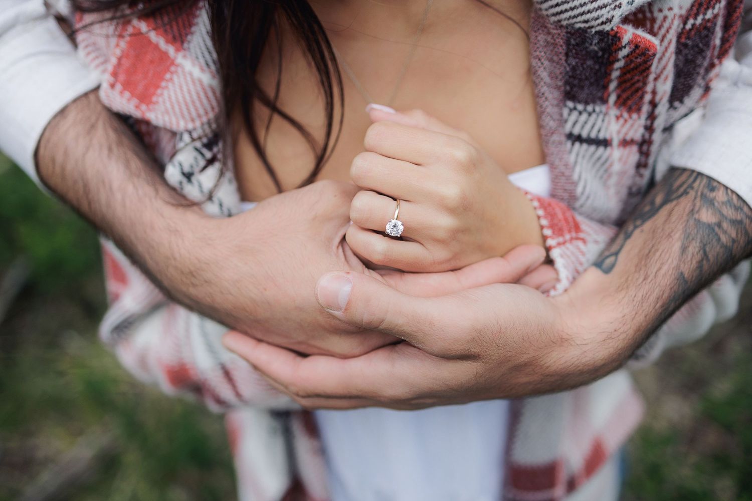 Close-up view of hands wearing an engagement ring on a ivory and coral colored floral dress.