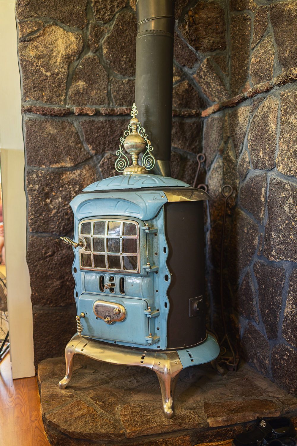 Vintage blue and gold cast iron wood stove with ornate details against a stone wall.