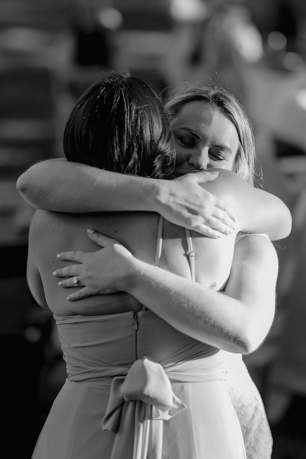 Two people share a tender emotional embrace in formal attire, captured in black and white photography.