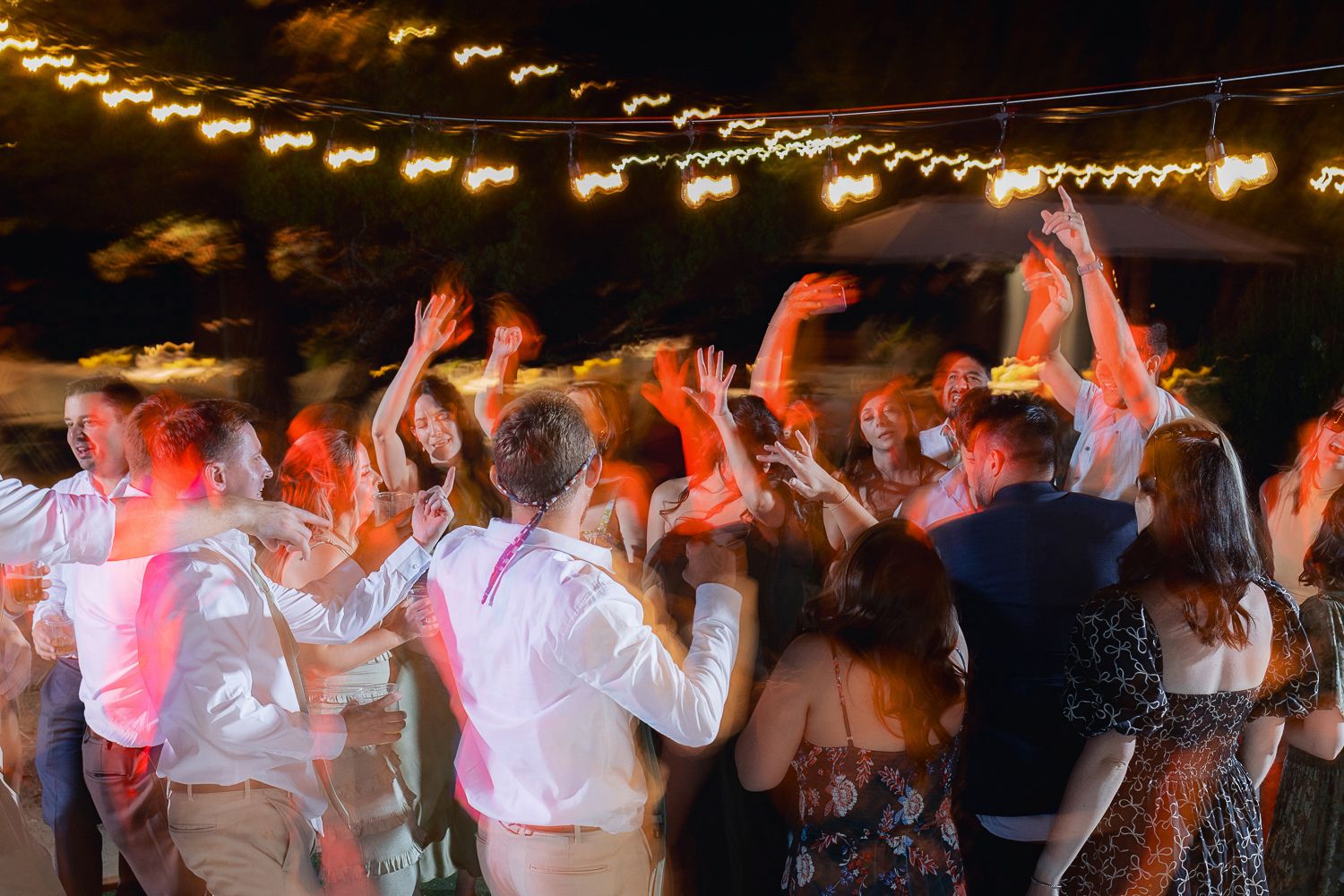 Dancing silhouettes of people celebrating under glowing string lights at a nighttime outdoor event.