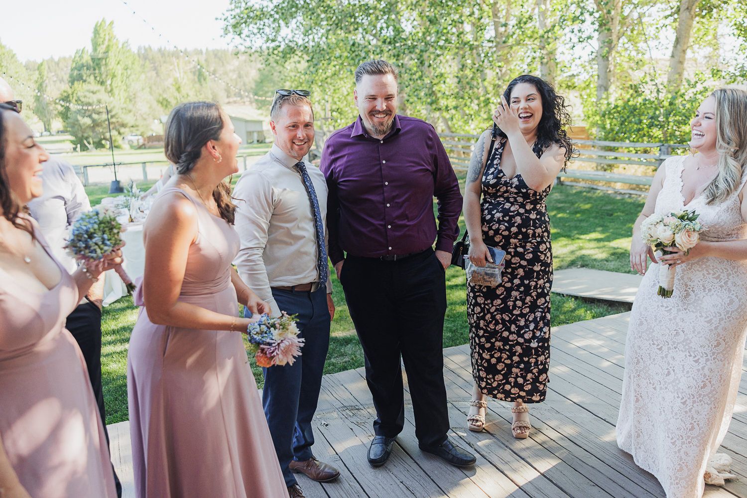 Wedding guests gather outdoors at a sunny garden venue for group photos and celebrations.
