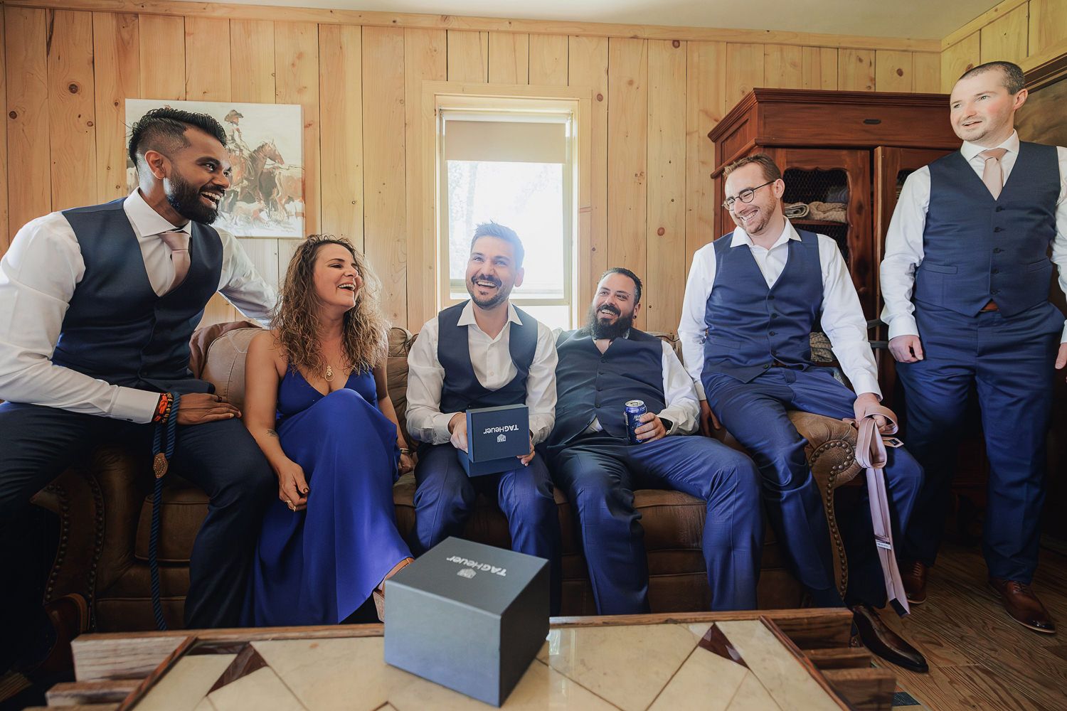 Wedding party members dance and celebrate in a rustic wood-paneled room during a reception.