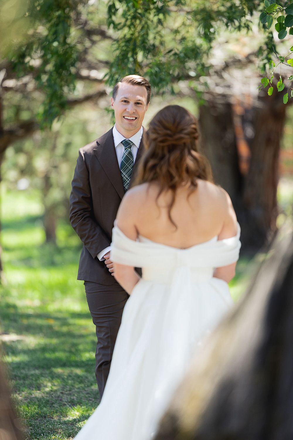 A couple sharing a playful first look wedding moment in a sun-dappled outdoor setting.