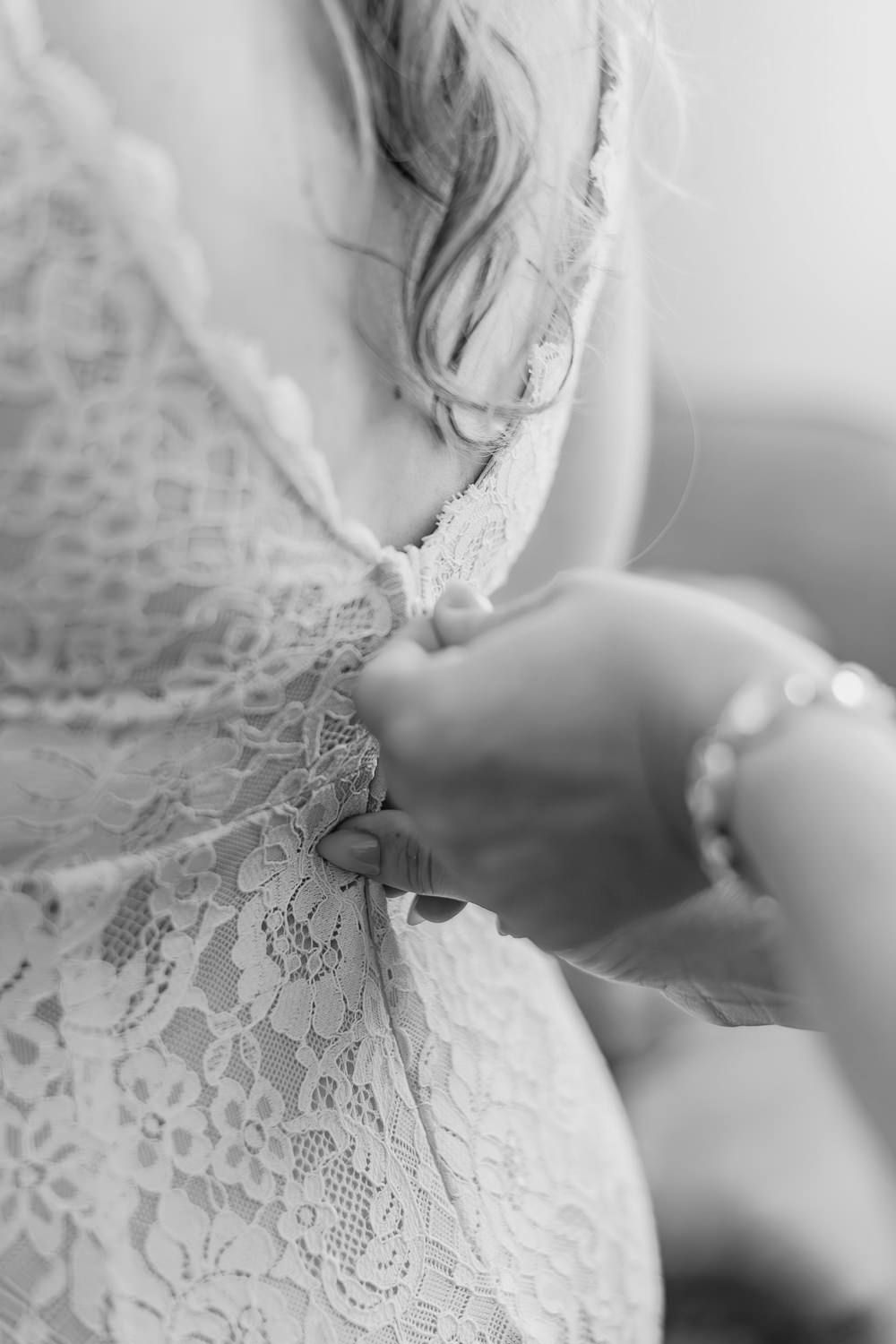Close-up black and white photo of delicate lace detail being fastened on a wedding dress.