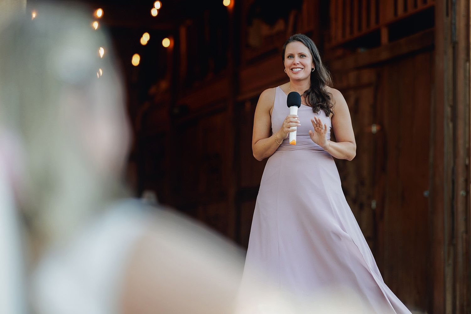 A bride and groom dance together at their wedding reception in a rustic barn venue with warm lighting.