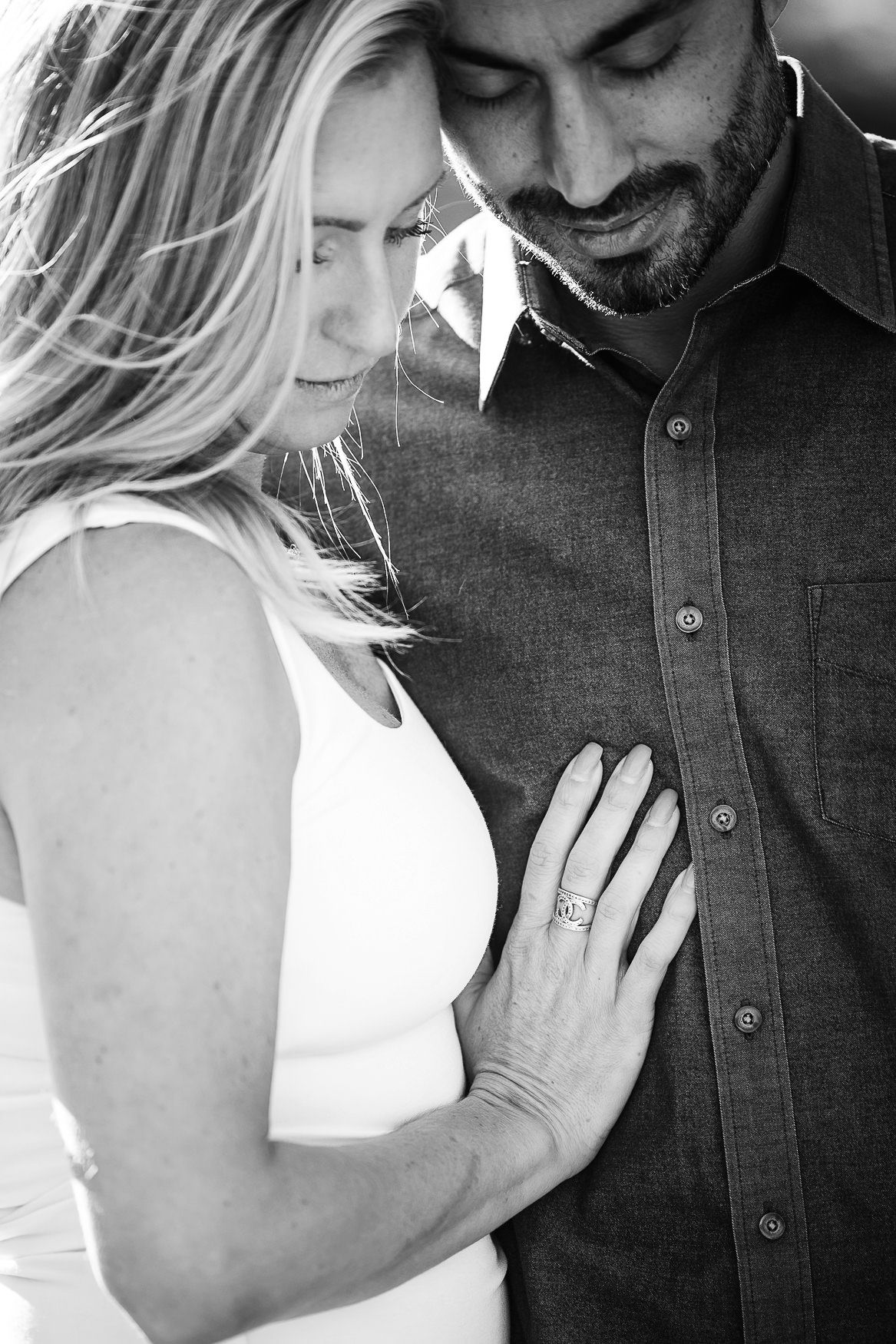 A tender black and white engagement photo shows a couple in an intimate embrace with her hand displaying the ring.