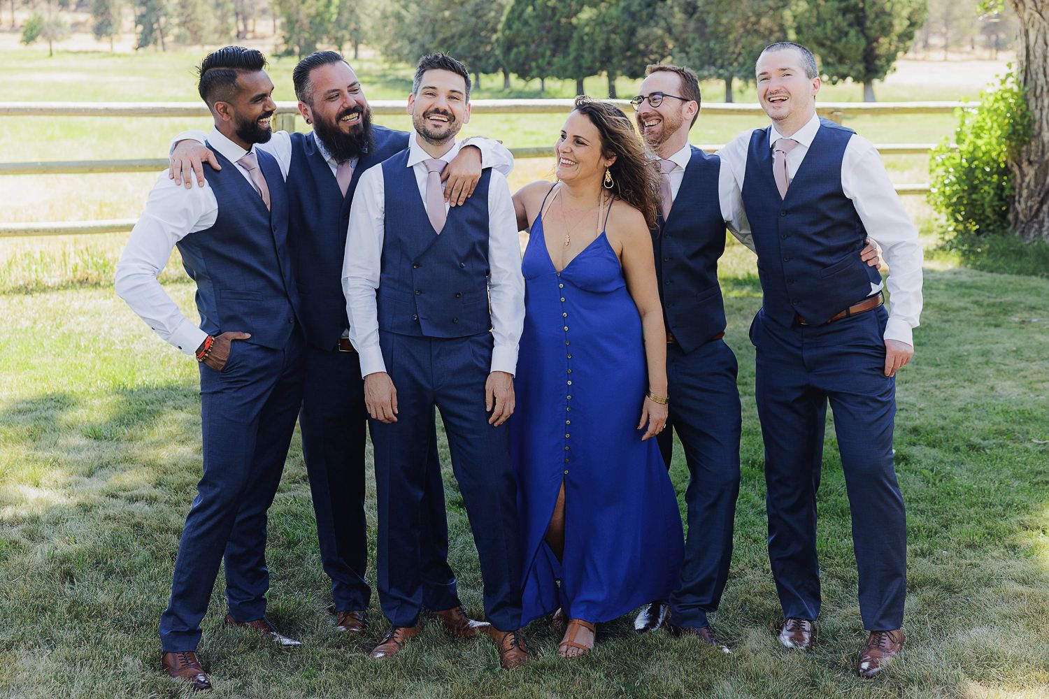 Wedding party in coordinating navy attire with one member in a royal blue dress pose together on a sunny lawn.