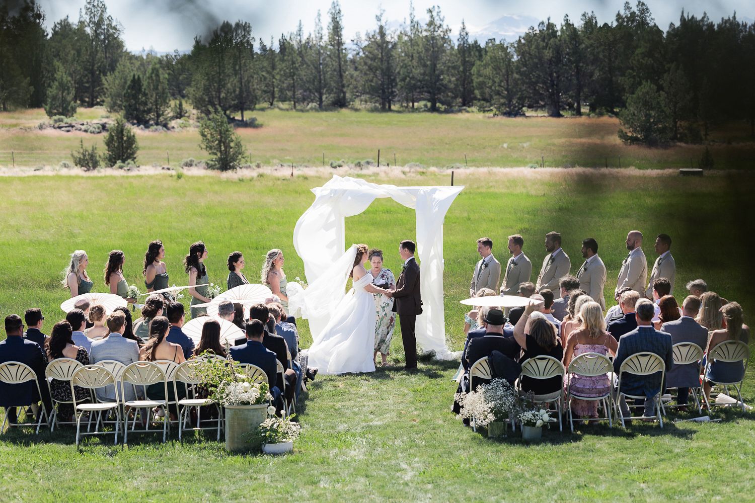 Guests seated outdoors for a rustic country wedding ceremony with evergreen trees and mountains in the background.