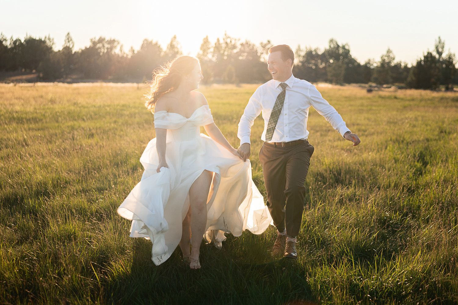 A couple runs through a golden meadow at sunset, with the bride's white dress flowing in the breeze.