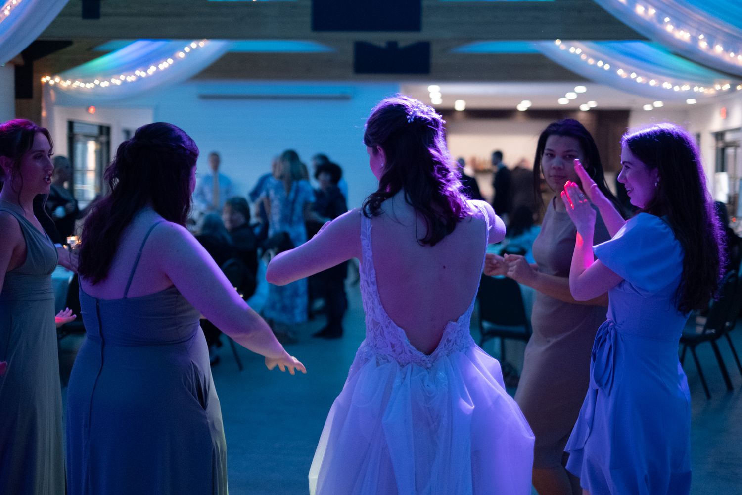 Wedding guests dancing together under blue lighting at an evening reception.