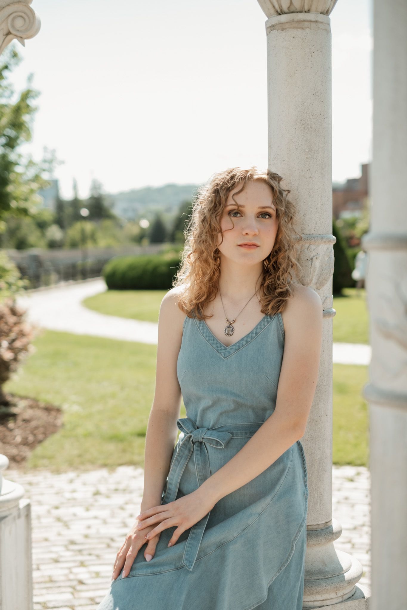 Four connected images show someone in a flowing blue dress posing elegantly against white stone columns outdoors.
