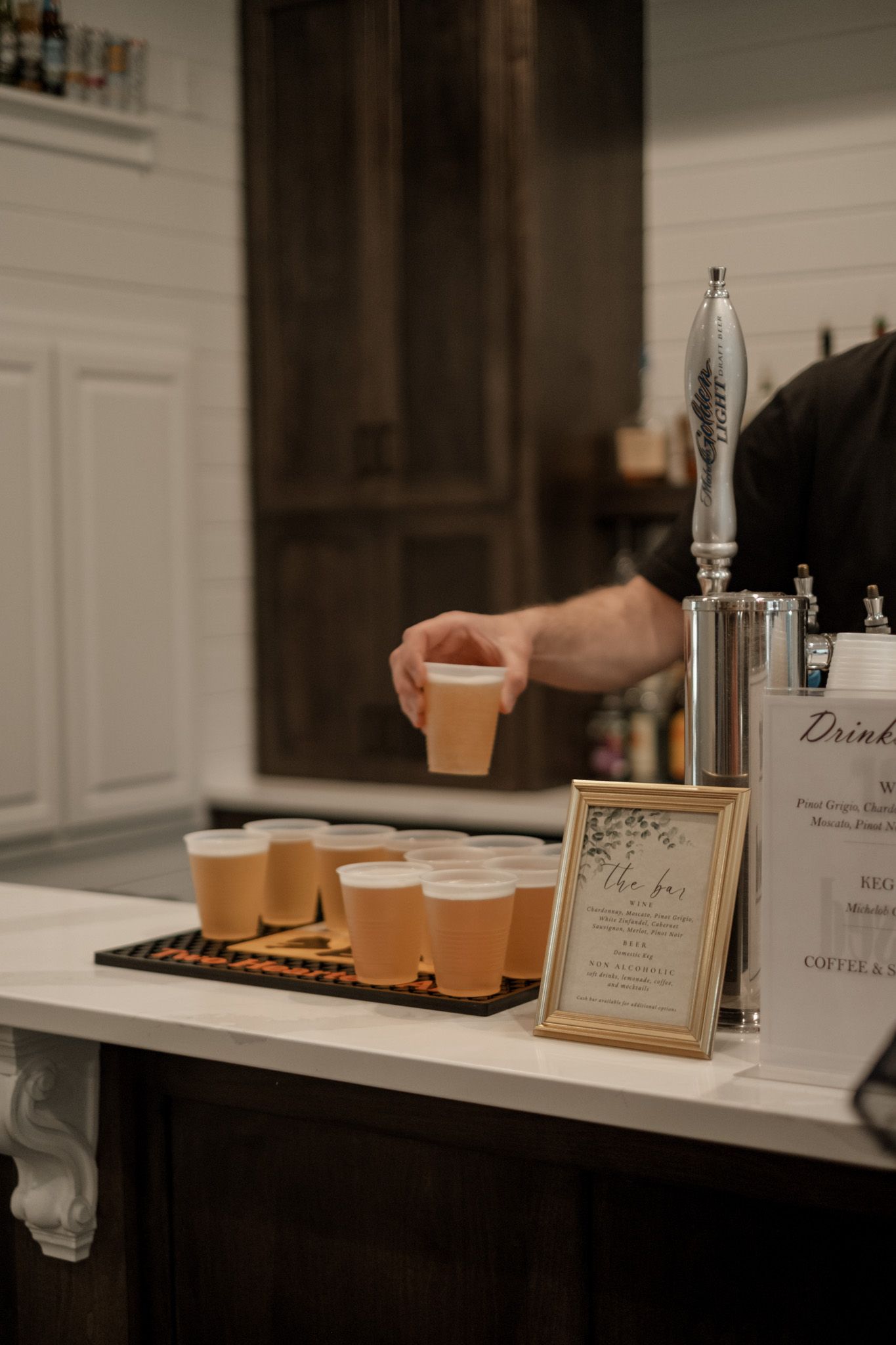 A drink station at a wedding reception with coffee cups and a framed menu on display.