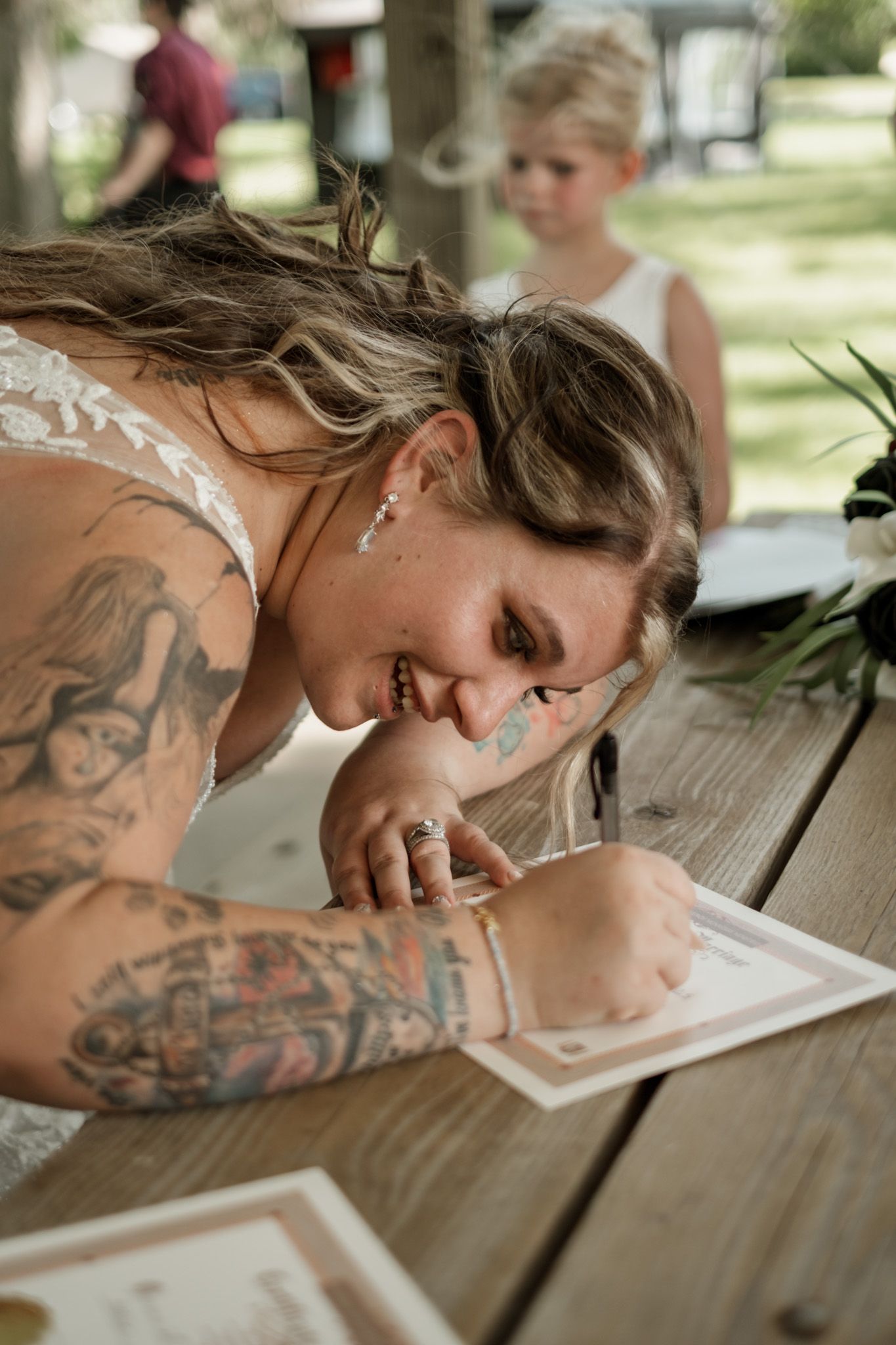 Sequence of shots showing someone signing documents on a wooden picnic table with visible tattoos.