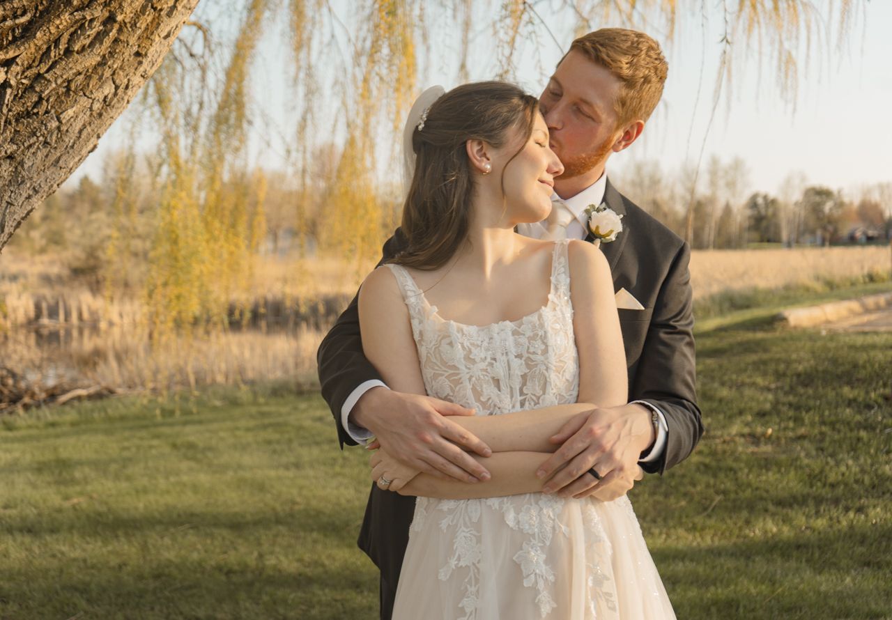 A romantic outdoor portrait of a couple embracing under a willow tree during golden hour.