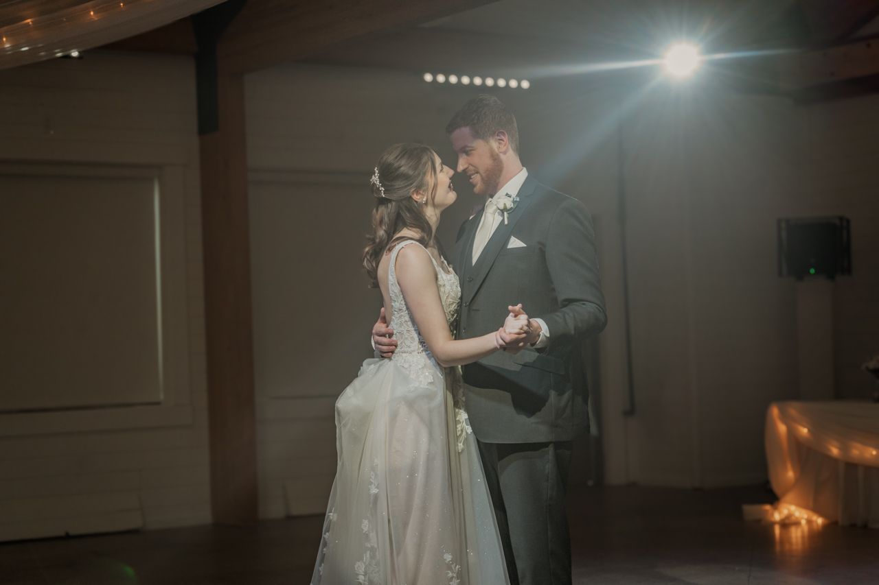 A couple shares their first dance under soft lighting at their wedding reception.