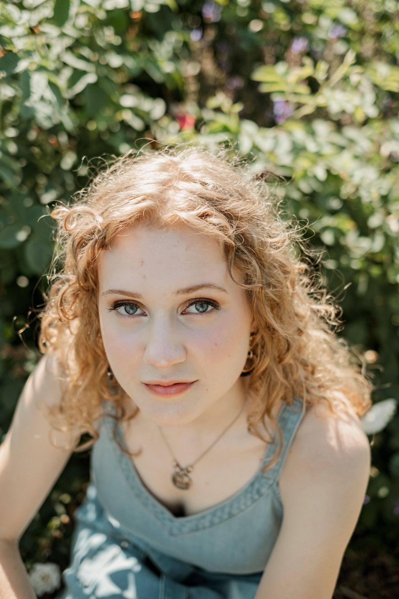 Closeup portrait series showing curly hair and blue eyes against lush greenery in natural lighting.