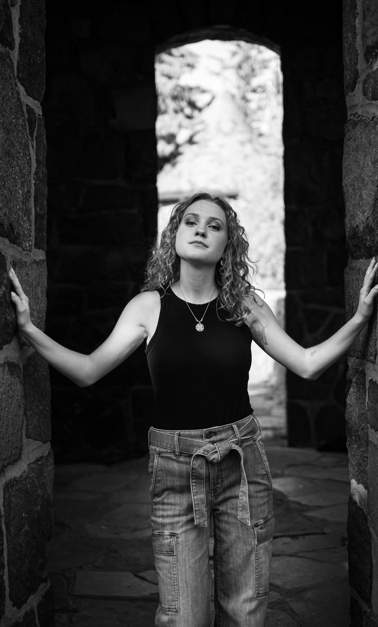 Someone leans against vertical stone pillars in black and white artistic portrait composition.