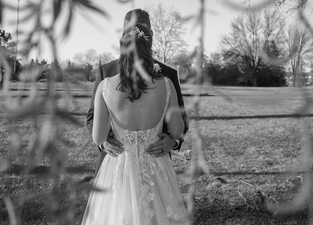 Black and white portrait of a bride in a lace wedding dress viewed through foliage.