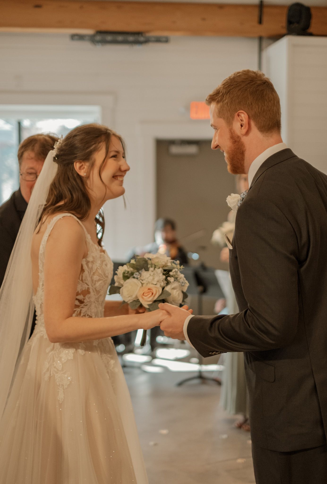 A joyful couple shares a candid moment during their wedding ceremony in a bright indoor venue.
