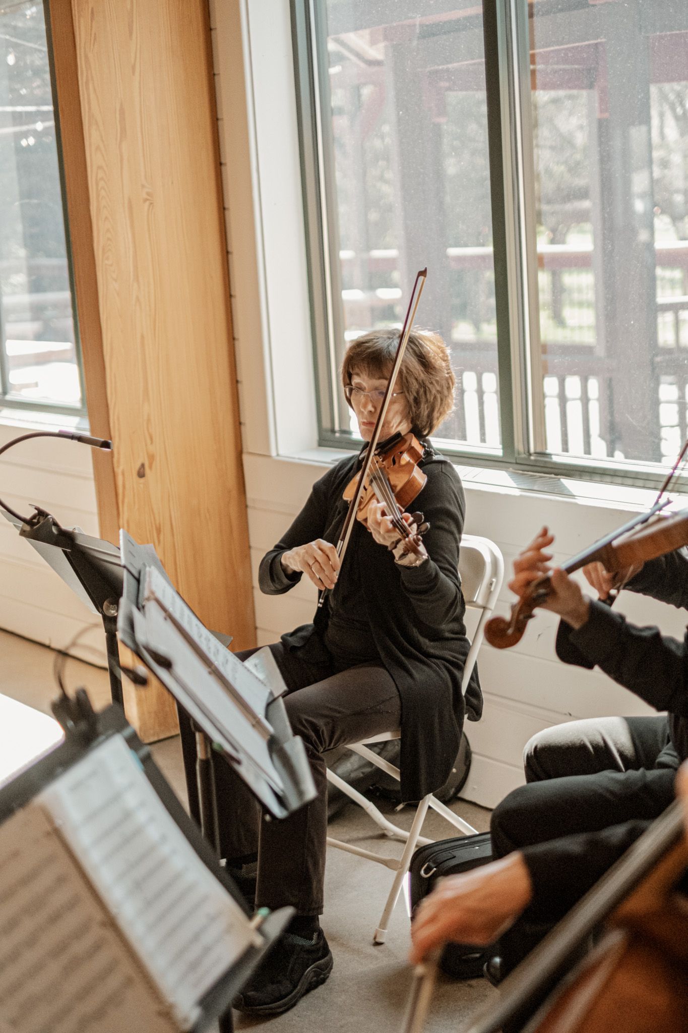 Classical musicians performing in a bright sunlit room with sheet music stands.