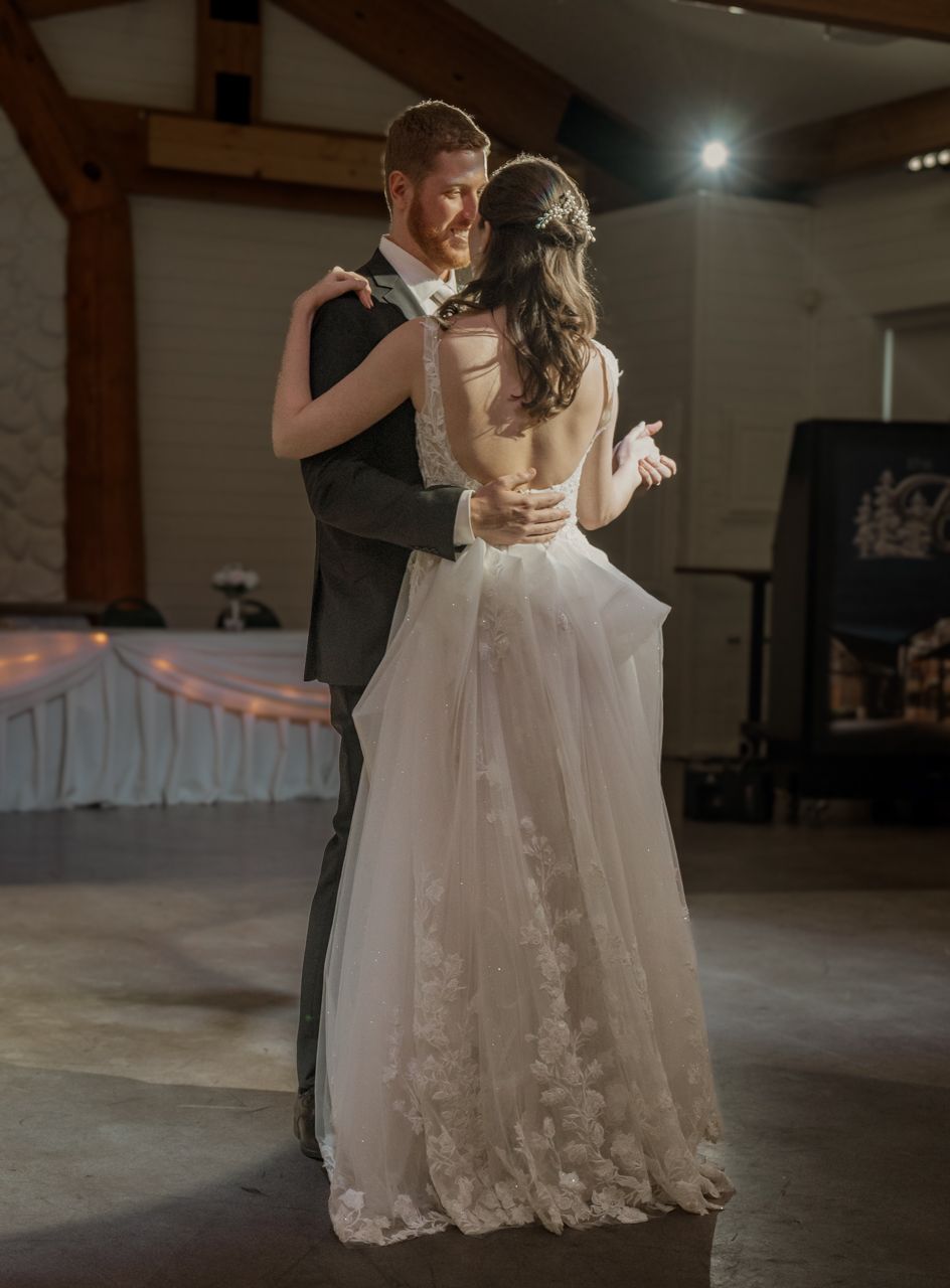 A couple shares their first dance in an elegant reception hall with exposed wooden beams.
