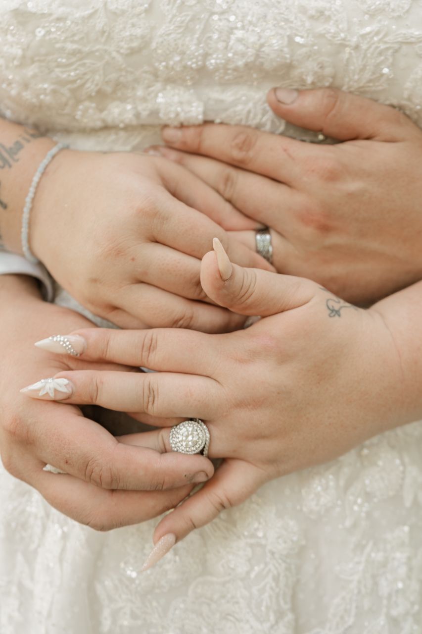 Close up photos of hands wearing engagement rings and wedding bands on lace fabric background at different angles.
