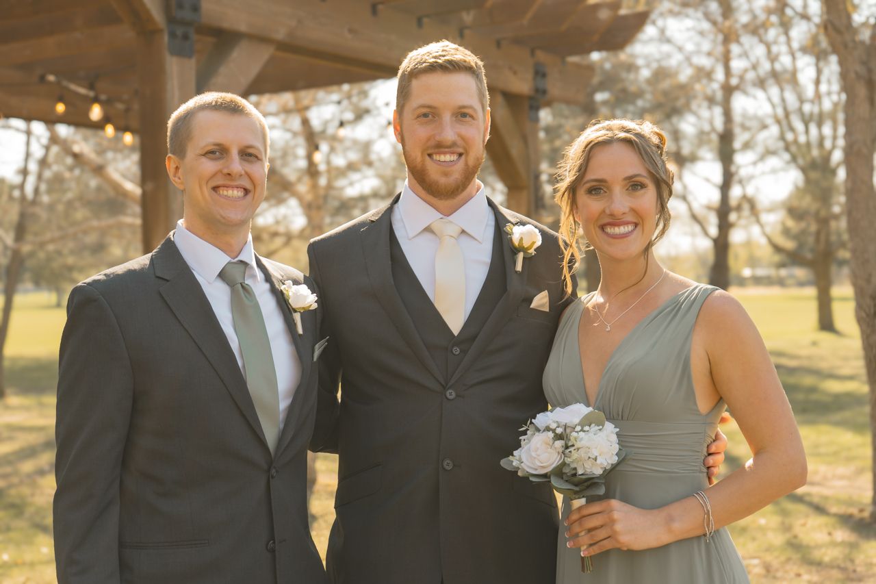 Wedding party trio poses together during golden hour outdoors.